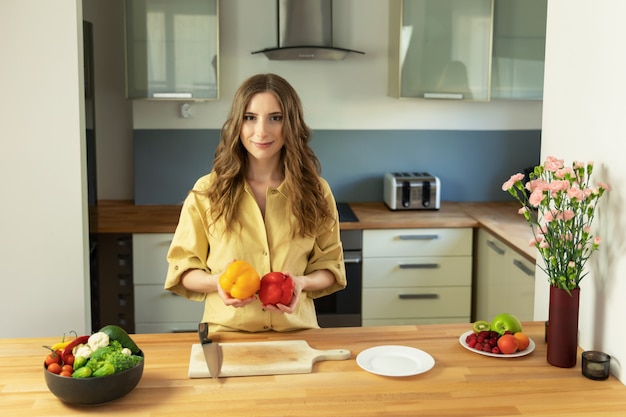 Young beautiful girl holding a sweet pepper in her hands. A woman prepares a salad of fresh, healthy vegetables.