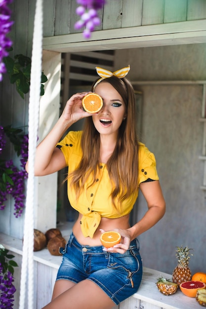 写真 トロピカルフルーツと明るい黄色の服を着た若い美しい少女