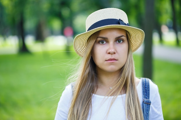 デニムのオーバーオールと公園を歩いている軽い帽子の若い美しい少女