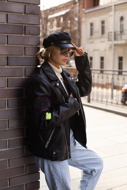 Фото Молодая красивая девушка в модной одежде с очками и черной шляпе на улице