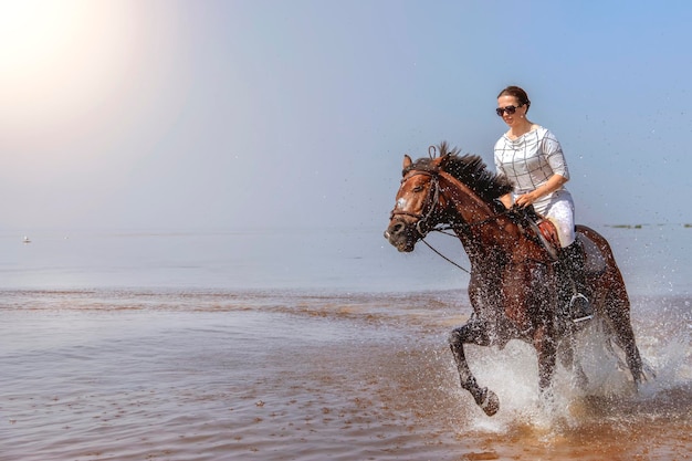 Young beautiful girl is galloping very fast on the water on a hot sunny day