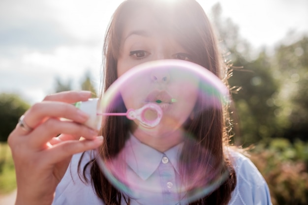 Молодая красивая девушка играет с мыльных пузырей в парке.