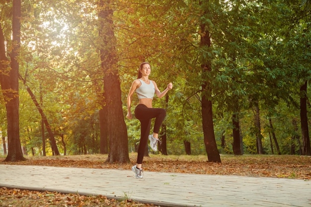 A young beautiful girl is running into the park on cool season at park