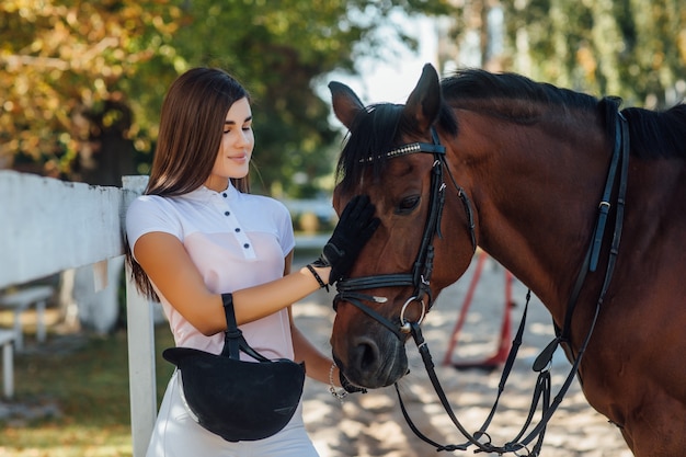 A young beautiful girl jockey with a horse in the park preparing for the competition