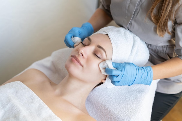 A young beautiful girl lies on the table at the beautician and receives facial cleansing procedures, makeup removal with white wipes