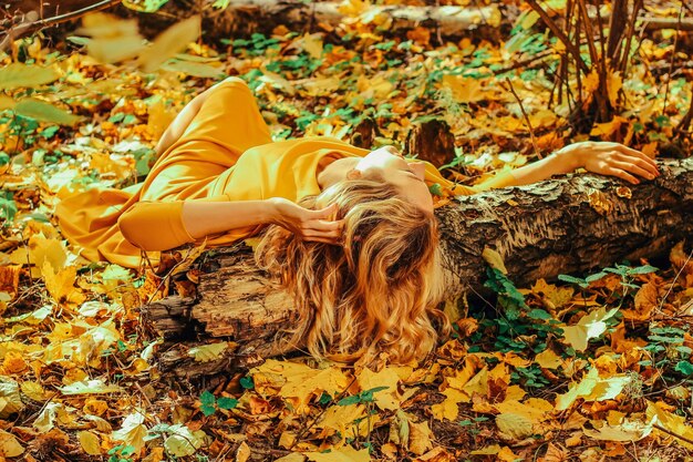 Photo young beautiful girl in a long yellow dress lying on the ground of the autumn park