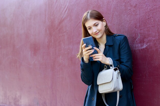 La giovane bella ragazza esamina lo smartphone,