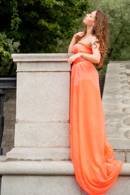 Photo a young beautiful girl poses in a red dress in the park