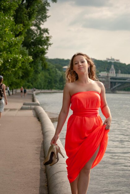 A young beautiful girl poses in a red dress in the park