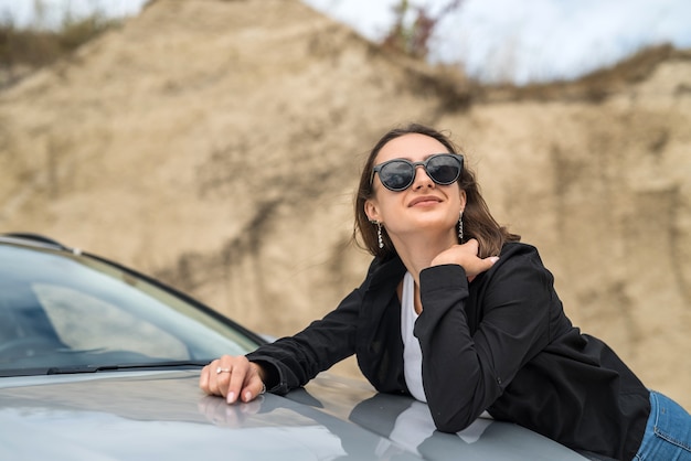 Young beautiful girl posing in a car on the nature traveling the country summer vacation