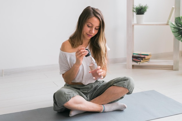 Young beautiful girl practicing yoga at mat drinking water while break Fitness and healthy lifestyle concept