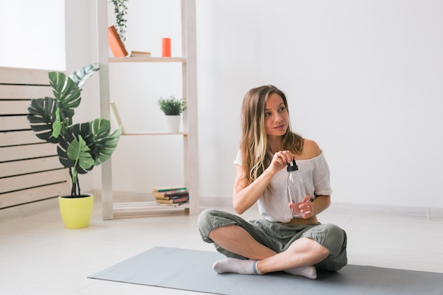 Young beautiful girl practicing yoga at mat drinking water while break fitness and healthy lifestyle