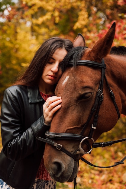 Young beautiful girl presses her head against a brown horse