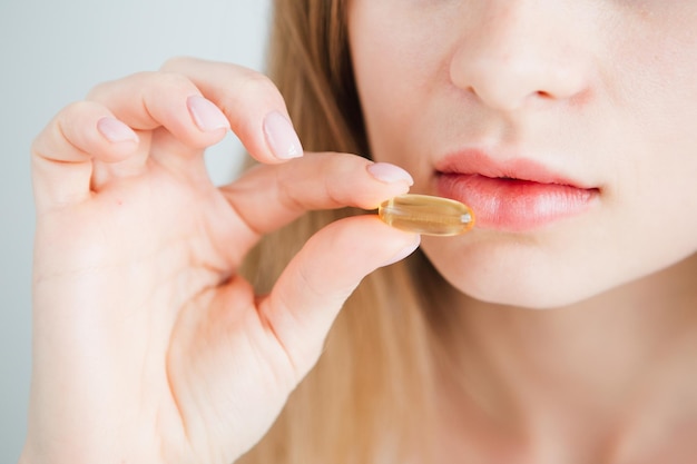 Young beautiful girl puts a pill in her mouth. Multicolored capsules tablets, vitamins, dietary supplements. Face close-up. Toning.