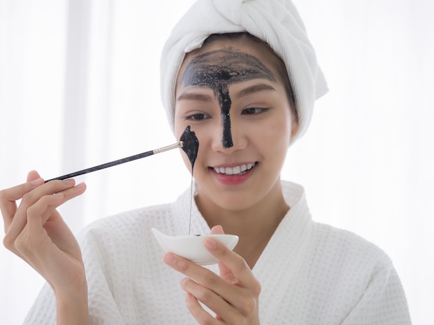 Young beautiful girl receiving black facial mask Attractive girl with moisturizing facial mask