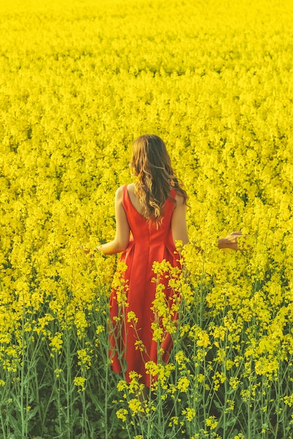 Young beautiful girl in a red dress close up in the middle of the yellow field with the radish flowers. Spring season