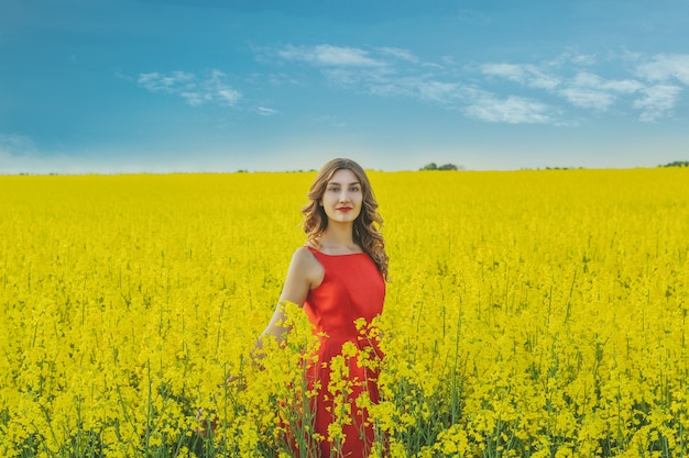 Young beautiful girl in a red dress close up in the middle of the yellow field with the radish flowers. Spring season