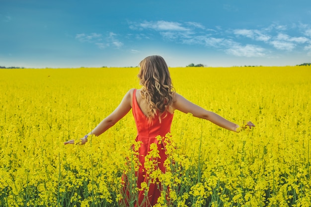 Young beautiful girl in a red dress close up in the middle of the yellow field with the radish flowers. Spring season