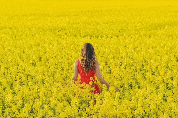빨간 드레스에서 젊은 아름 다운 소녀 무 꽃과 함께 노란색 필드 중간에 닫습니다. 봄 기간