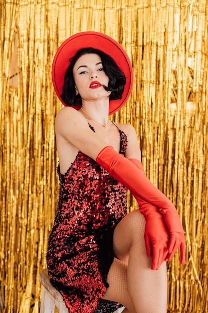 Young beautiful girl in a red dress and hat posing on a gold background