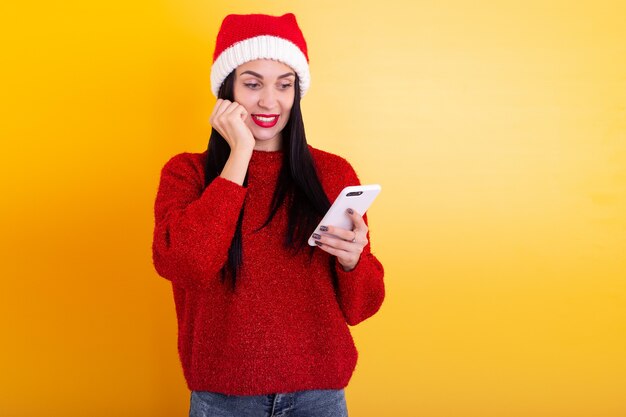Young beautiful girl in a red Santa hat holds a phone in his hands