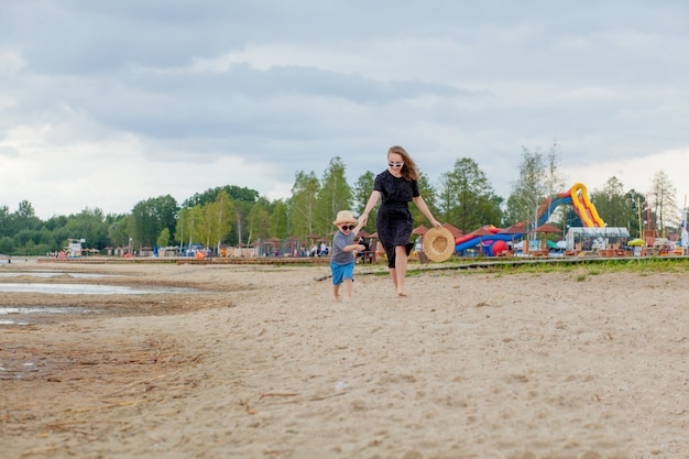 A young beautiful girl runs along a sandy beach in the sea with her son