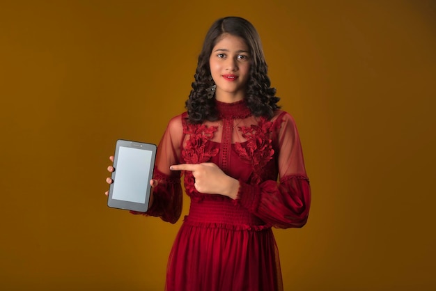 Young beautiful girl showing a blank screen of a smartphone or mobile or tablet phone on a brown background