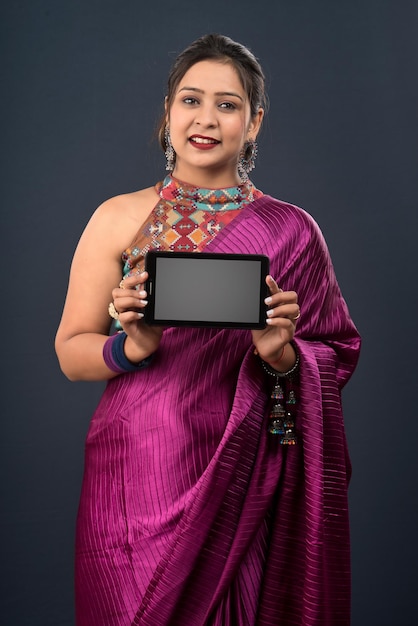 Young beautiful girl showing a blank screen of smartphone or mobile or tablet phone on a grey background