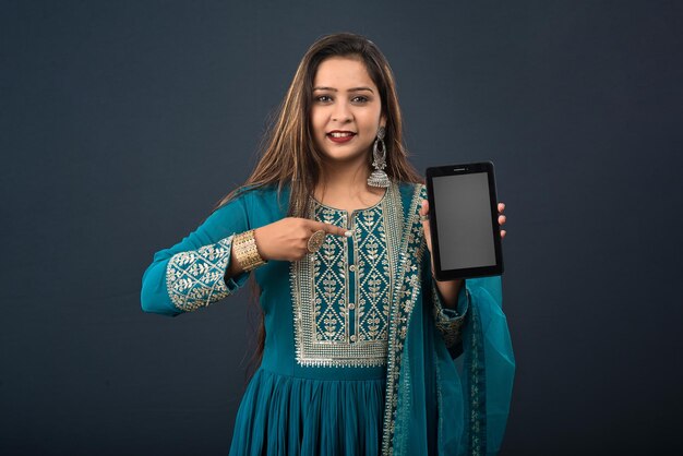 Молодая красивая девушка показывает пустой экран смартфона или мобильного или планшетного телефона на сером фоне