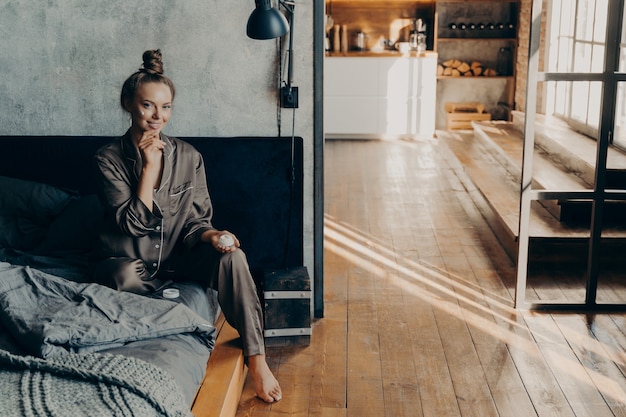 Young beautiful girl sits on bed in pajamas after waking up