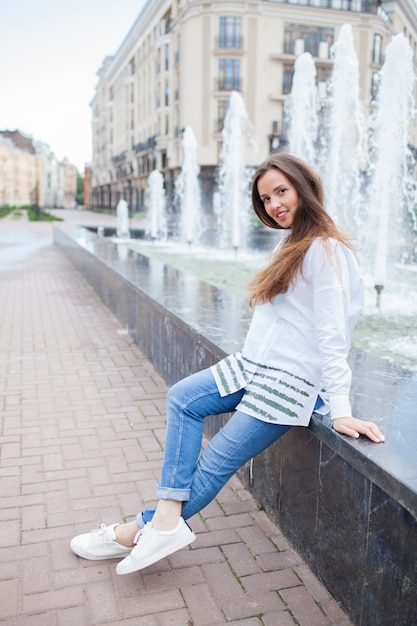 Young and beautiful girl sitting at the fountain.