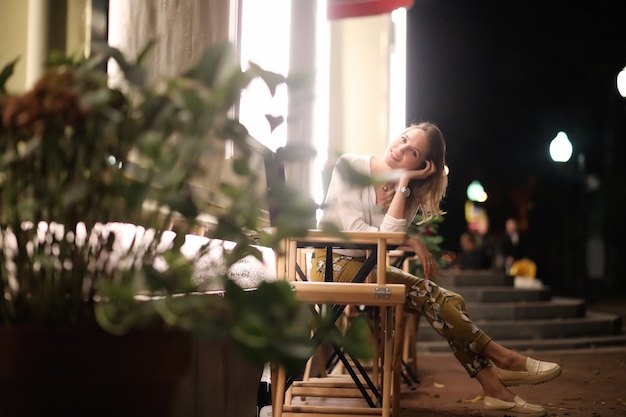 Young beautiful girl sitting in a street cafe at night