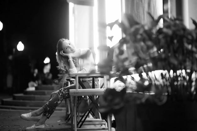 Young beautiful girl sitting in a street cafe at night