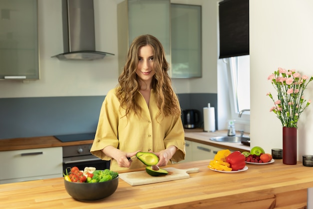 Young beautiful girl slices ripe avocado. A woman prepares a salad of fresh, healthy vegetables.