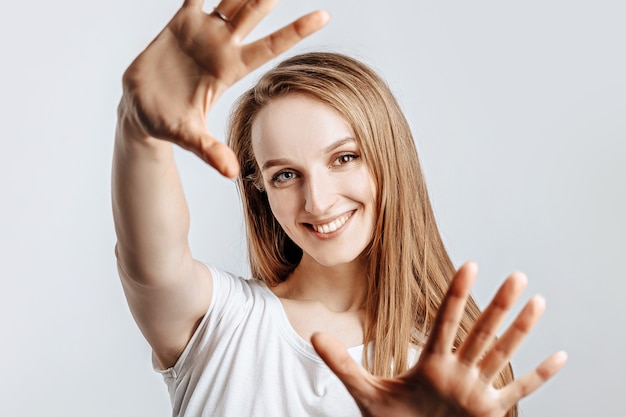 Young beautiful girl smiling and pulling her hands towards camera on gray isolated background