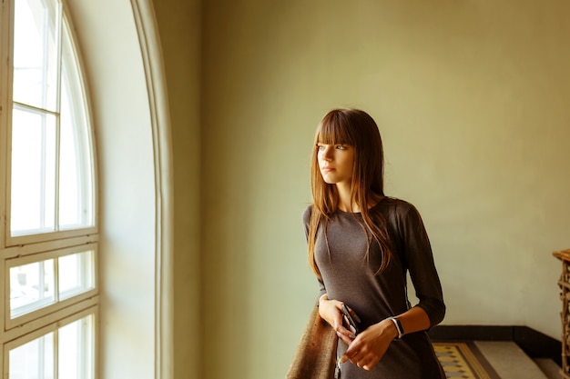 Young beautiful girl standing near the window smiling.