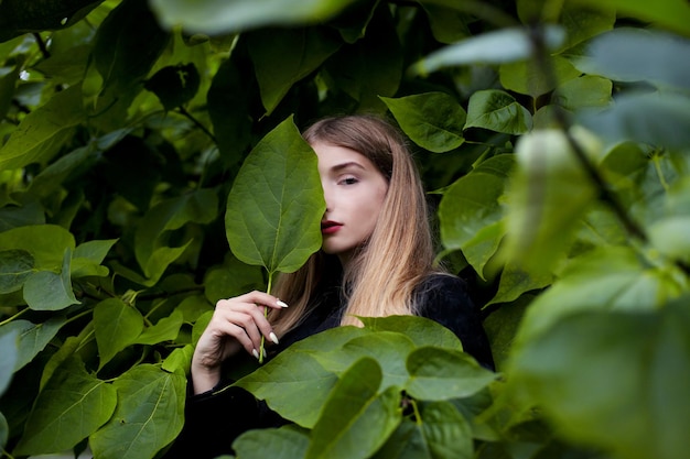 Young beautiful girl stands near a wall of leaves