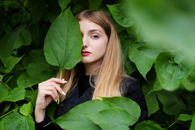 Young beautiful girl stands near a wall of leaves
