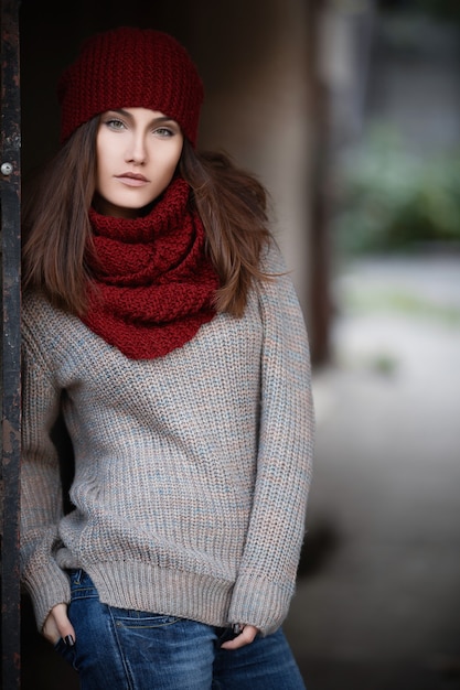 Foto giovane e bella studentessa con una sciarpa rossa con un maglione lavorato a maglia e un cappello e uno zaino