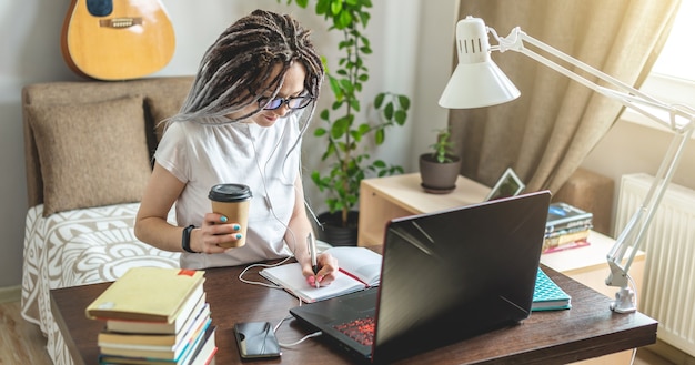 Photo a young beautiful girl student with dreadlocks is studying at an online lesson at home on a laptop