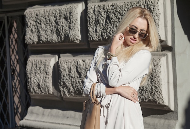 Young beautiful girl in stylish sunglasses and with a fashionable bag at sunset.