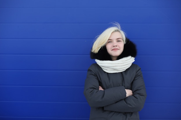 青い壁の背景で冬の散歩に若い美しい女の子