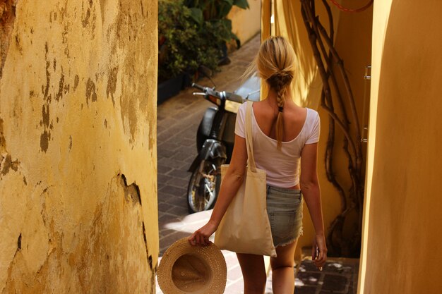 Young beautiful girl walks along the narrow street of greece in the summertime