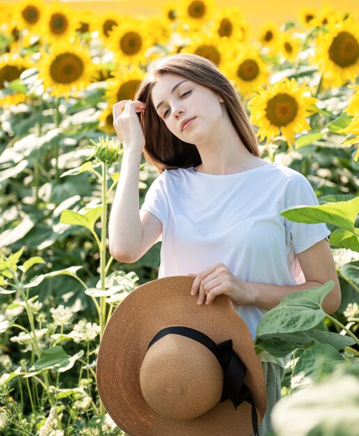 若い美しい少女は、咲くひまわりのあるフィールドで夏に歩きます