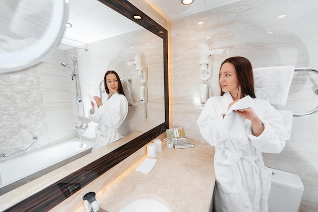 A young beautiful girl washes her face and holds a towel in a beautiful white bathroom A fresh good morning at the hotel Rest and travel Hotel recreation and tourism