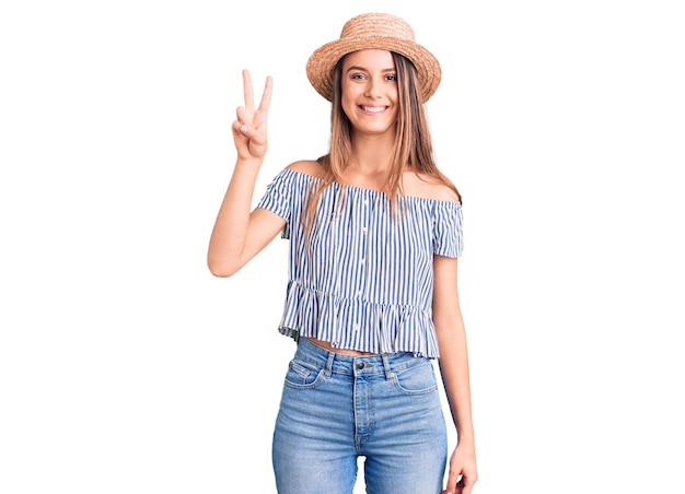 Young beautiful girl wearing hat and t shirt showing and pointing up with fingers number two while smiling confident and happy