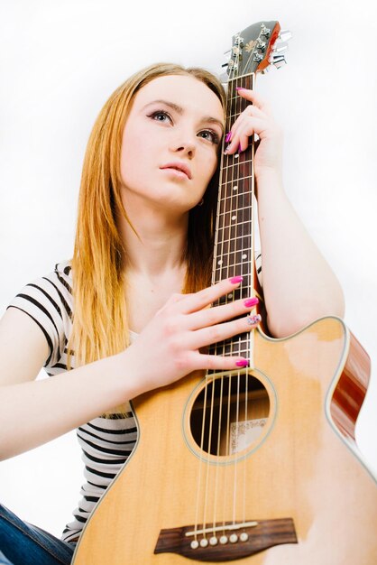 Young beautiful girl wearing jeans and a striped Tshirt with an acoustic guitar on a white background