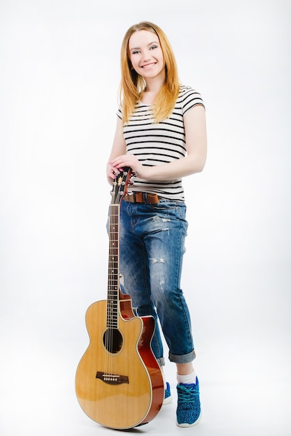 Young beautiful girl wearing jeans and a striped Tshirt with an acoustic guitar on a white background