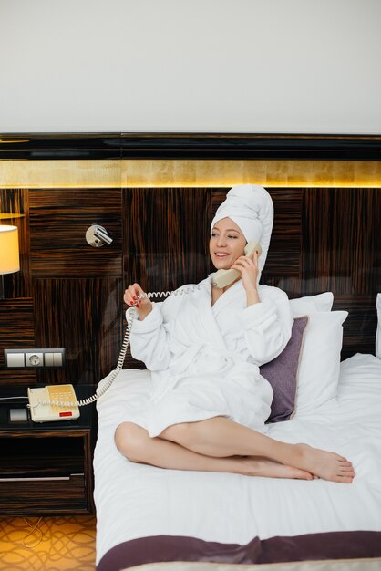 Foto una giovane bella ragazza in camice bianco sta parlando al telefono nella sua stanza d'albergo