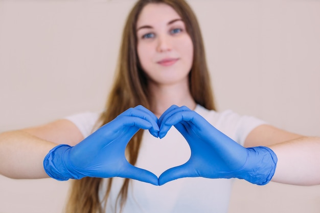 Молодая красивая девушка в белой футболке в синих перчатках, держась за руки в форме сердца